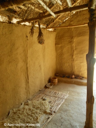 Το εσωτερικό ενός από τα σπίτια στο Δισπηλιό. Διακρίνεται ένα στρώμα από προβιά, αρωματικά φυτά κρεμασμένα από την οροφή και μαγειρικά σκεύη στο βάθος.